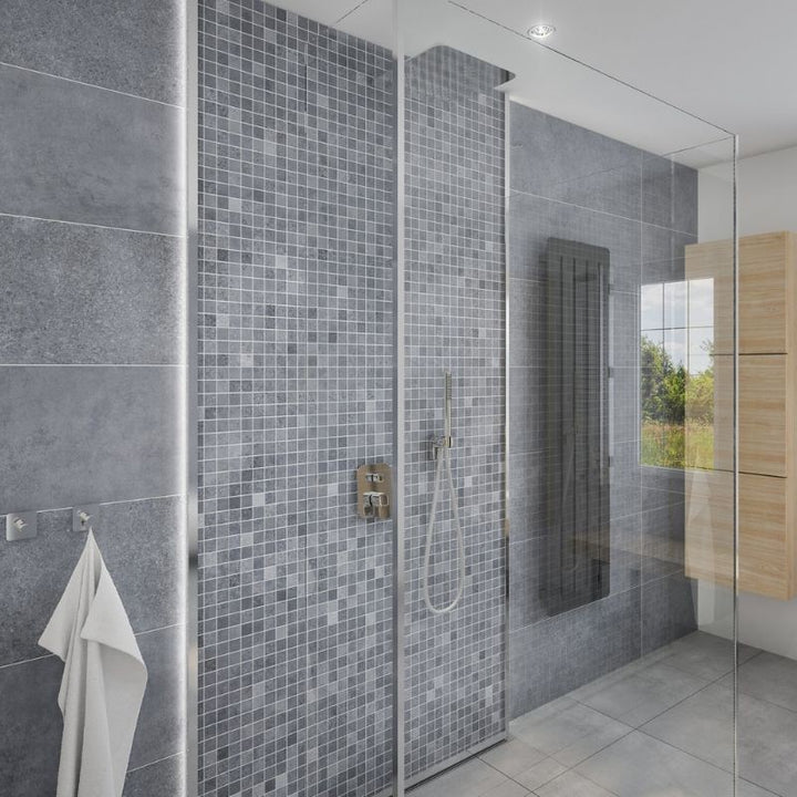 Modern bathroom interior with glass walk-in shower, small mosaic tiles, large gray stone tiles, chrome fixtures, wall-mounted towel holder, and a glimpse of wooden cabinet against a natural light backdrop.